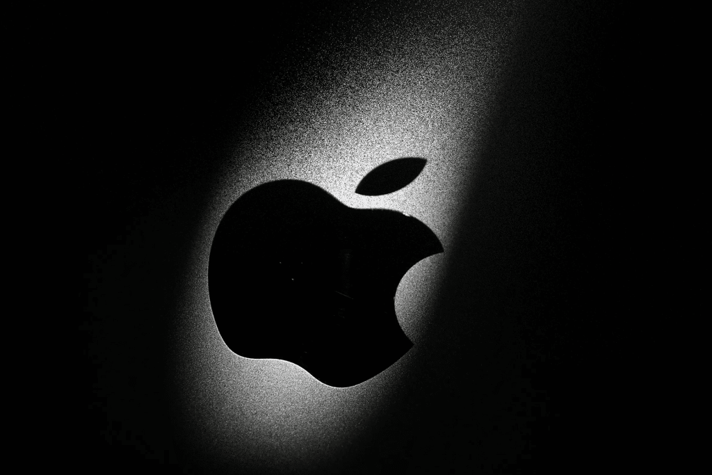 A close-up of a black Apple logo on a metallic surface, illuminated by a soft beam of light from the upper right, creating a dramatic shadow effect—an image reminiscent of Apple's $2 million bug bounty spotlight.