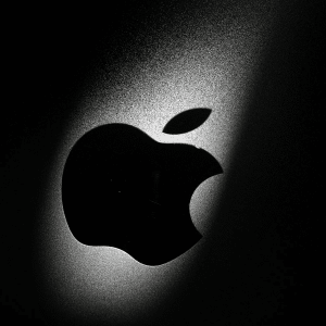 A close-up of a black Apple logo on a metallic surface, illuminated by a soft beam of light from the upper right, creating a dramatic shadow effect—an image reminiscent of Apple's $2 million bug bounty spotlight.