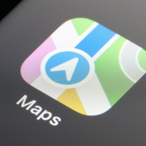 Apple Maps - Close-up of a smartphone screen showing the Maps app icon, which features a stylized map with a blue navigation arrow. The word "Maps" appears below the icon, hinting at possible Apple Maps ads in 2026.