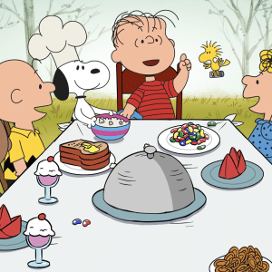 A group of Peanuts characters sit around a table outdoors, enjoying desserts, candy, sandwiches, and pretzels. Snoopy dons a chef’s hat as Woodstock flies above, bringing classic charm to the Apple TV holiday lineup.