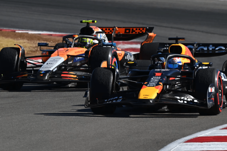 Two Formula 1 cars race closely around a bend on the track, their vibrant colors captured in stunning detail. This thrilling moment could be seen on the latest Apple F1 broadcast deal, with both helmeted drivers pushing to the limit.