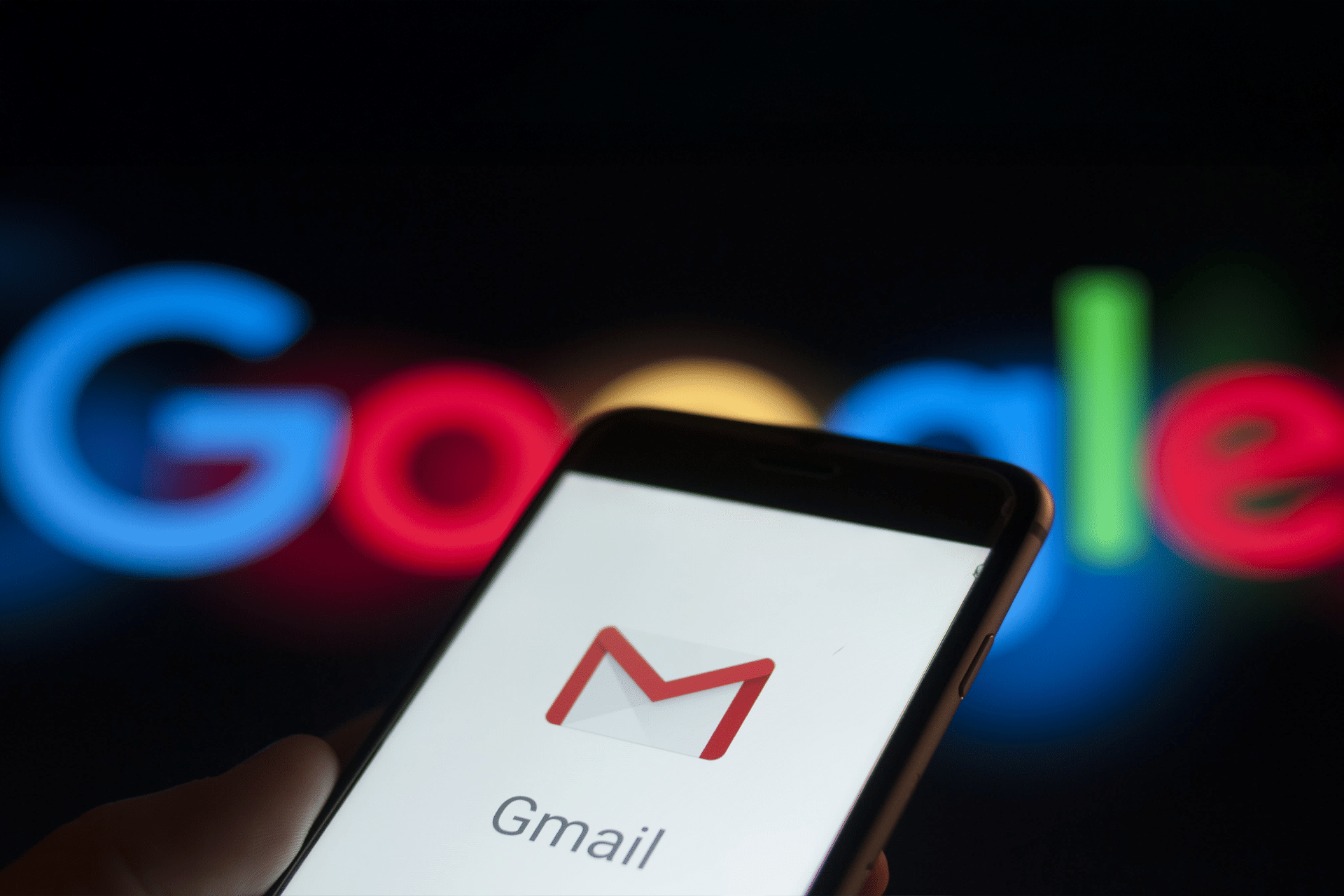 A smartphone displaying the Gmail logo and app name is held in front of a blurred Google logo in the background, highlighting concerns following a recent Gmail data breach.