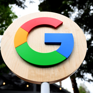 A round wooden sign featuring the colorful Google "G" logo in red, yellow, green, and blue stands out against trees and a blurred outdoor background, evoking thoughts of Google and Amazon cloud contracts in Israel.