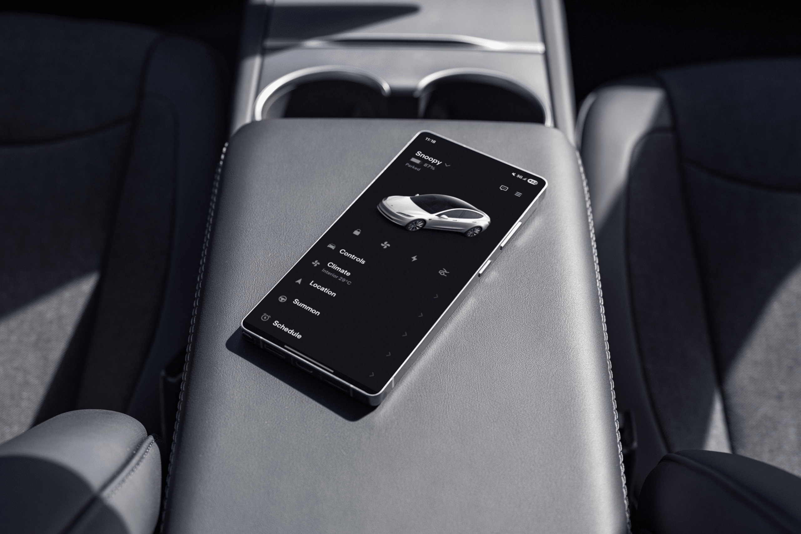 A smartphone displaying a car control app rests on the center armrest inside a modern 2026 Tesla Model 3, with gray seats and cup holders visible in the background.