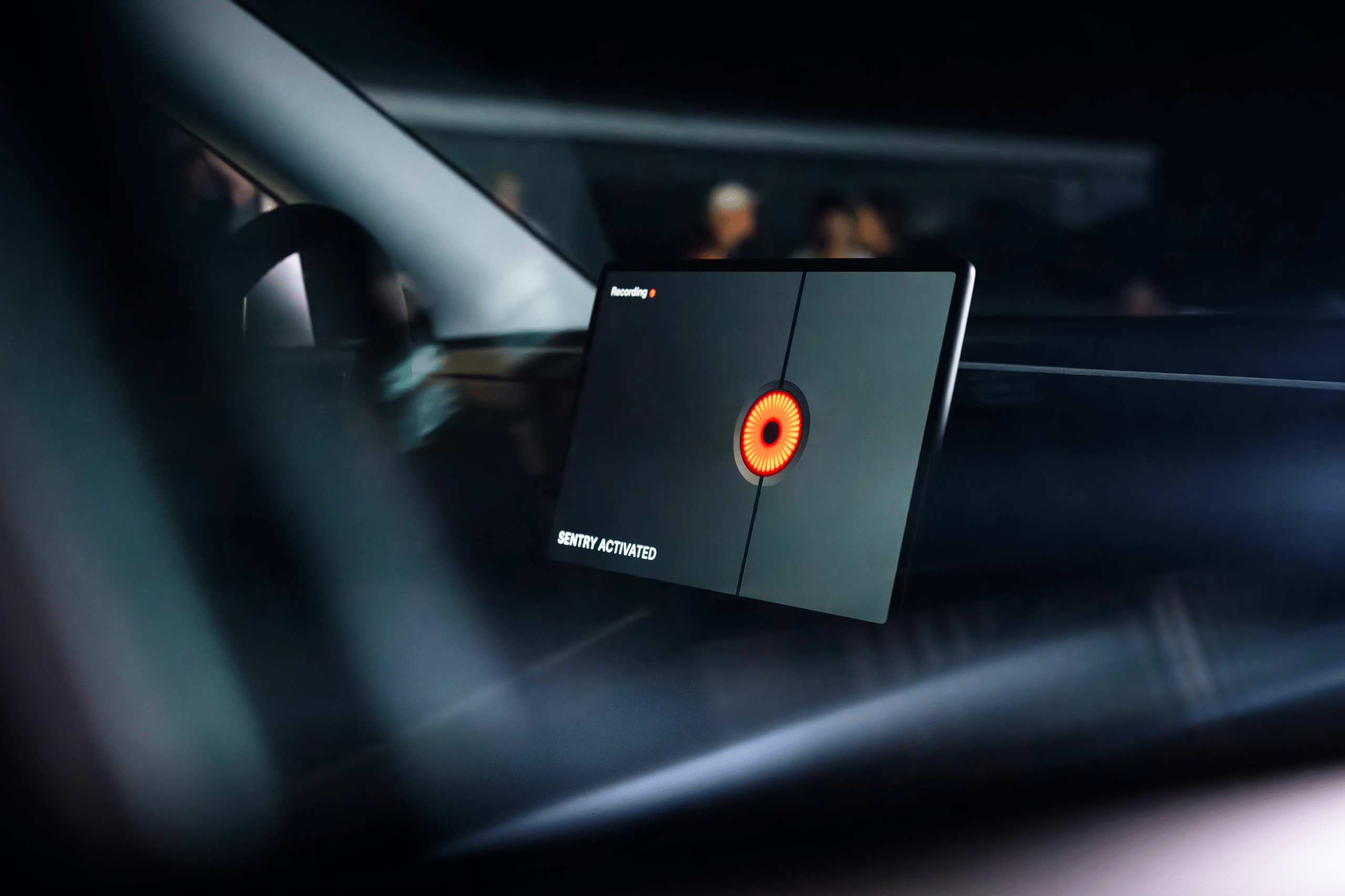 A close-up of a 2026 Tesla Model 3 dashboard screen displays a red circular graphic and the words "IDENTITY ACTIVATED," with a dark interior and blurred figures visible through the windshield.