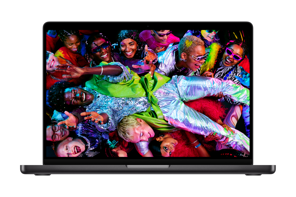 A 14-inch MacBook Pro with the new M5 chip displays a vibrant image of a lively group of people in colorful, shiny outfits, cheering and celebrating in a festive atmosphere.