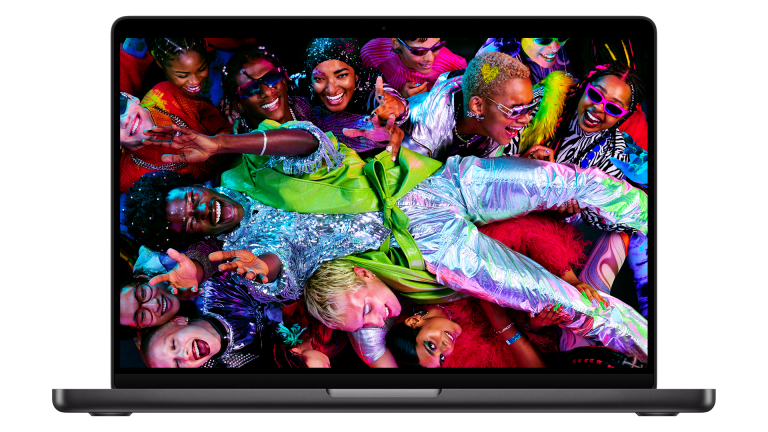 A 14-inch MacBook Pro with the new M5 chip displays a vibrant image of a lively group of people in colorful, shiny outfits, cheering and celebrating in a festive atmosphere.