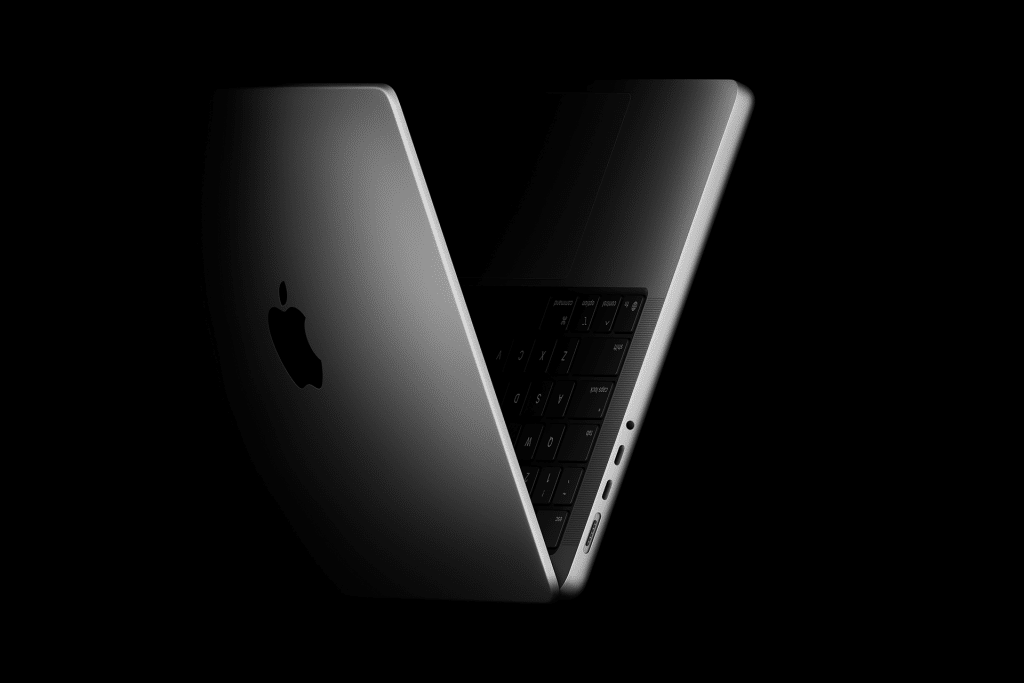 A partially open, silver 14-inch MacBook Pro M5 chip on a black background, showing the keyboard, screen hinge, and multiple side ports, with the Apple logo visible on the lid.