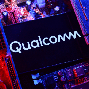 A close-up photo of a smartphone displaying the Qualcomm logo, surrounded by various computer circuit boards and illuminated with red and blue lighting, highlights the power behind Qualcomm AI chips.