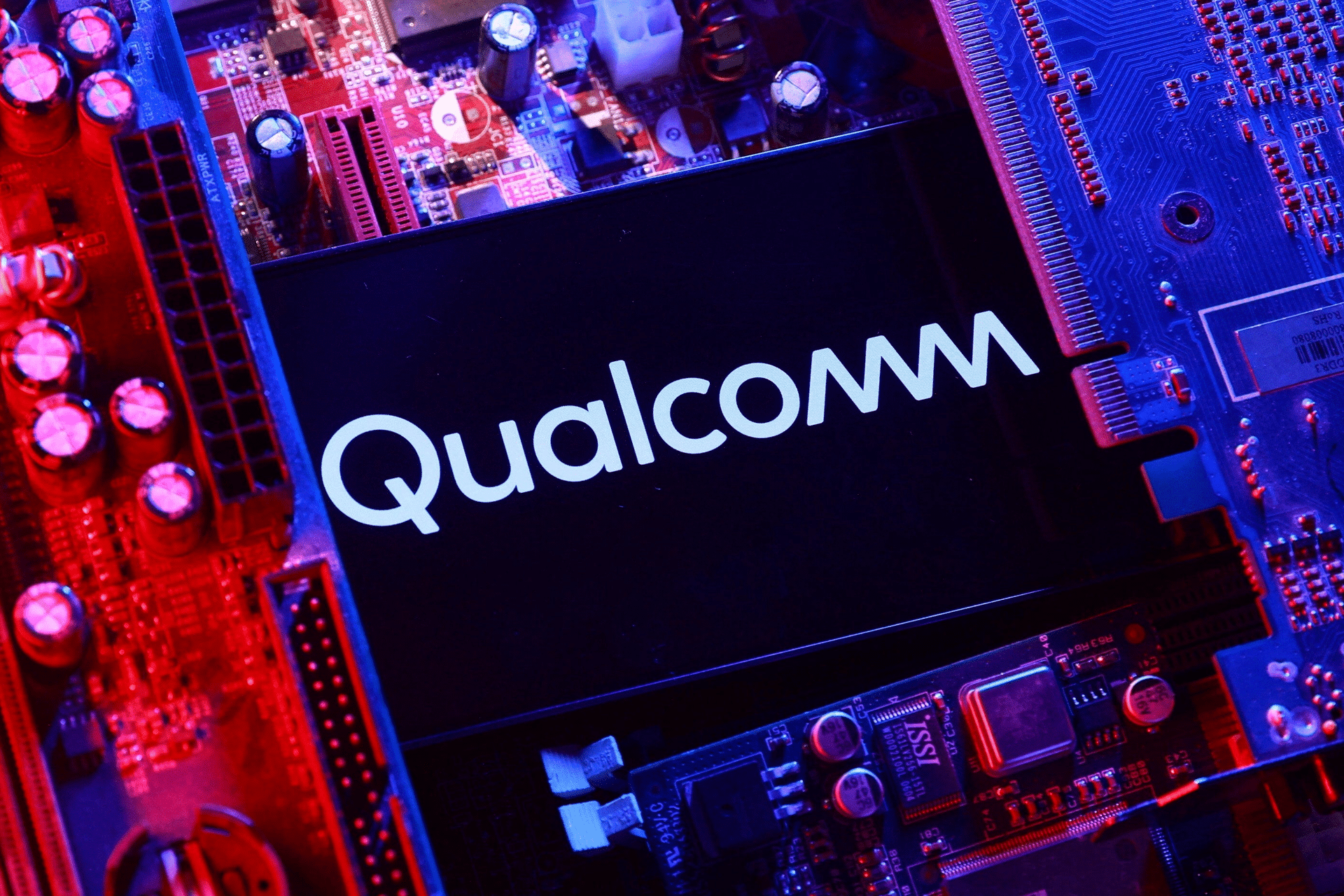 A close-up photo of a smartphone displaying the Qualcomm logo, surrounded by various computer circuit boards and illuminated with red and blue lighting, highlights the power behind Qualcomm AI chips.