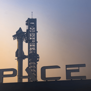 A SpaceX rocket stands on its launch pad at sunset, the large SpaceX sign visible in the foreground, as the sky fades from yellow to blue—hinting at innovations like the Globalstar SpaceX acquisition and Apple partnerships shaping space technology.