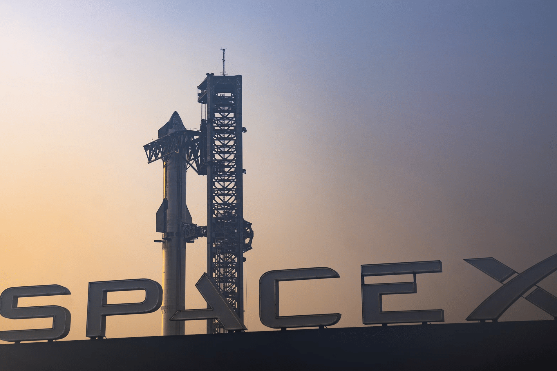 A SpaceX rocket stands on its launch pad at sunset, the large SpaceX sign visible in the foreground, as the sky fades from yellow to blue—hinting at innovations like the Globalstar SpaceX acquisition and Apple partnerships shaping space technology.