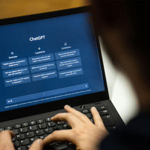 A person types on a laptop displaying the ChatGPT interface—ideal for computer science graduates exploring the job market—showing sections for Examples, Capabilities, and Limitations on a dark screen.
