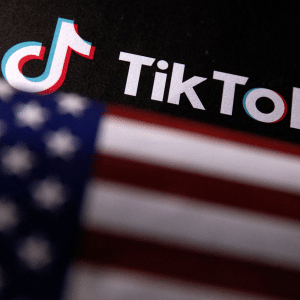 The TikTok logo and name are displayed on a black background, with a blurred American flag in the foreground—hinting at ongoing TikTok deal tensions between the U.S. and China.