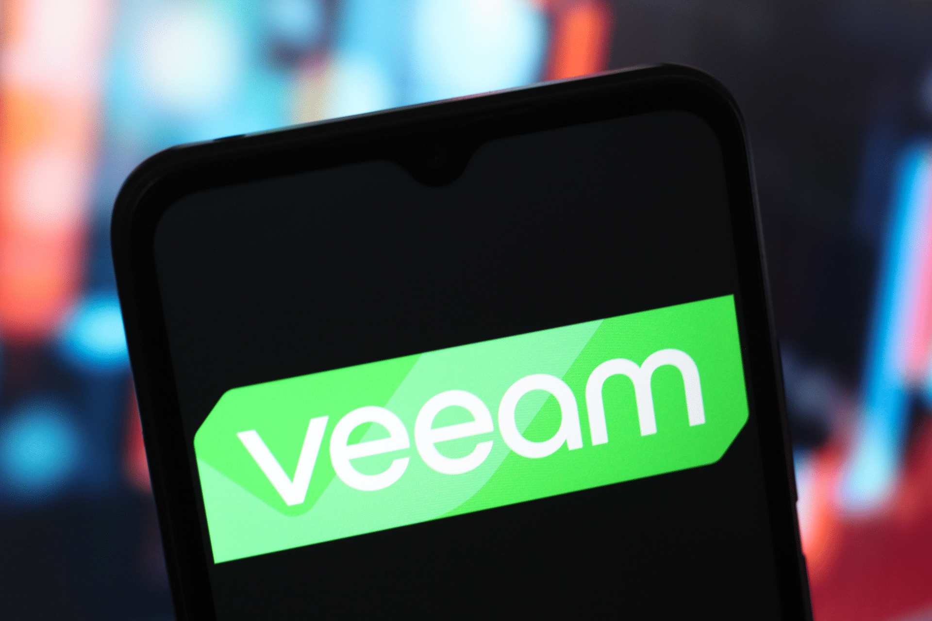 A smartphone screen displays the Veeam logo in white text on a green background, with a blurred colorful background behind the phone, highlighting news of Veeam acquiring Securiti.ai.
