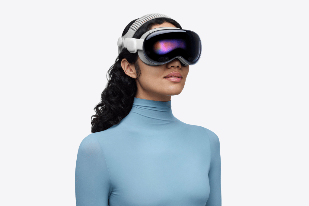 A person wearing a sleek Vision Pro headset powered by the advanced M5 chip and a light blue, long-sleeved turtleneck top stands against a plain white background.