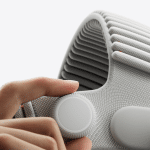 A close-up of a hand adjusting the round, white knob on the side of a textured, light-gray fabric strap, possibly part of a modern electronic device like the Vision Pro with its advanced M5 chip.
