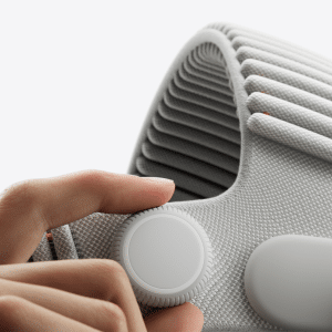A close-up of a hand adjusting the round, white knob on the side of a textured, light-gray fabric strap, possibly part of a modern electronic device like the Vision Pro with its advanced M5 chip.