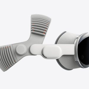 Side view of a sleek, modern virtual reality headset featuring the advanced Vision Pro M5 chip, with a white and gray fabric strap, rounded edges, and a smooth, reflective front surface. The design is accented with orange details on the strap.