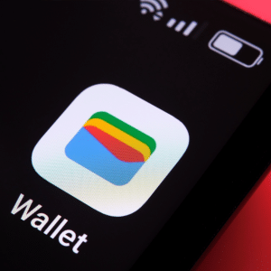 Close-up of a smartphone screen displaying the Google Wallet app icon, with vibrant layered shapes, and "Wallet" below. The phone rests on a red background—perfect for managing cards or Apple Wallet boarding passes on iOS 26 devices.