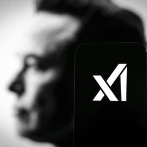 A smartphone displays the white X logo of the X social media app, hinting at xAI and AI-powered video game integration, with the blurred side profile of a man's face in the background.