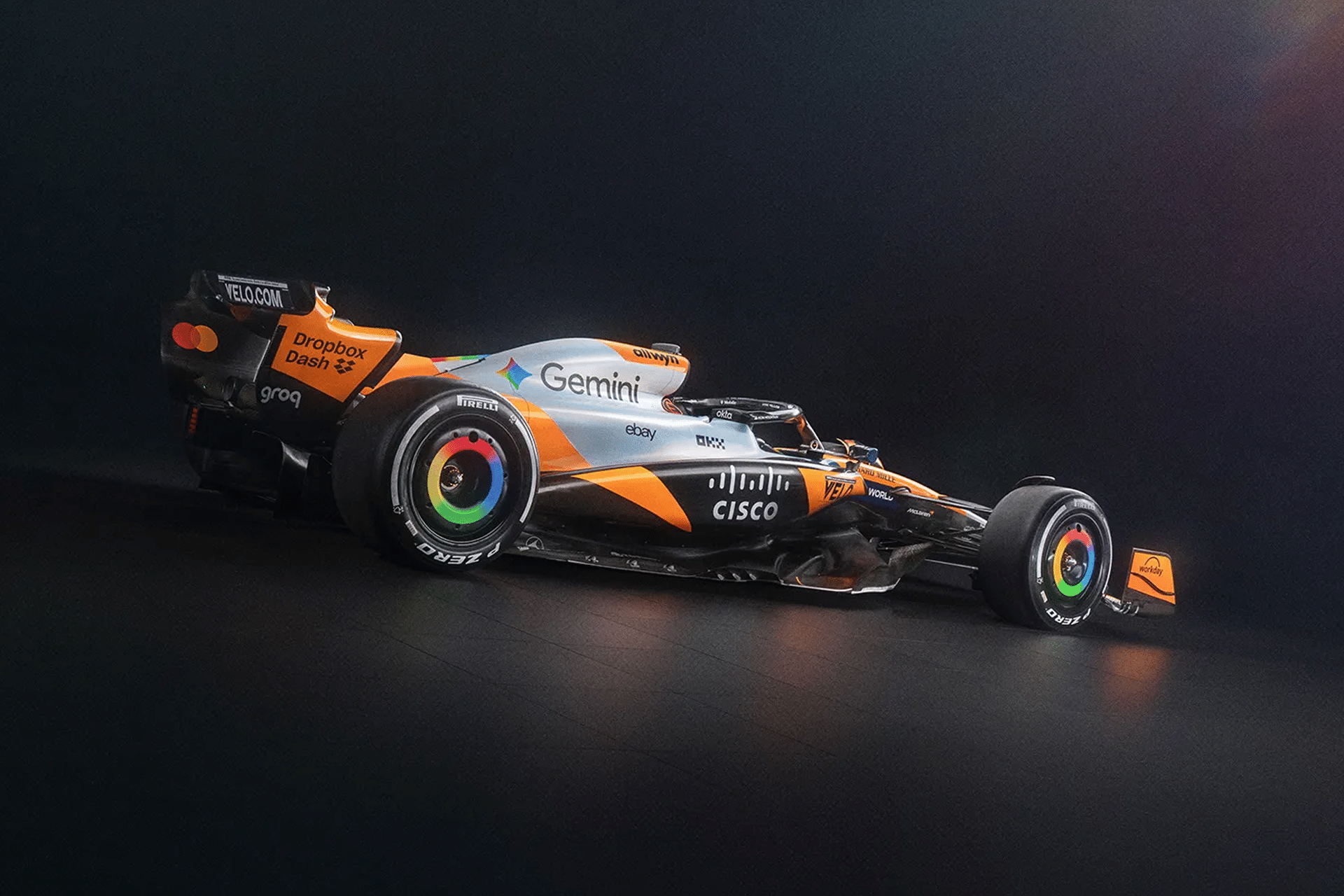 A McLaren Formula 1 car with orange, black, and silver livery is shown against a dark background, evoking a scene from F1 The Movie. Sponsor logos like Gemini, Cisco, and Dropbox stand out, along with vibrant wheel rims and aerodynamic detailing.