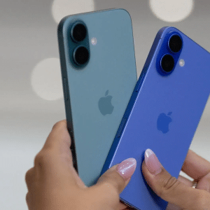 Two hands holding two different colored iPhones, one blue-green and one blue, both showing the Apple logo and dual rear cameras—devices like these are often targeted by stolen iPhone smuggling rings—against a blurred light background.