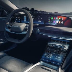 Modern electric car interior featuring a digital dashboard, steering wheel, and large touchscreens displaying controls, navigation, and apps. The Apple CarPlay interface is visible on the central display.