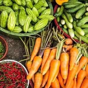 An assortment of fresh vegetables in baskets, including carrots, cucumbers, bitter melons, green chilies, and red chilies, displayed on a market floor highlights the importance of food plant sanitation services for maintaining freshness and safety.