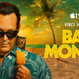 A man in sunglasses and a tropical shirt holds a popsicle on the beach at sunset, with a small monkey on his shoulder. Palm trees and a cooler are in the background. Text: "Apple TV+, Vince Vaughn, Bad Monkey Season 2.