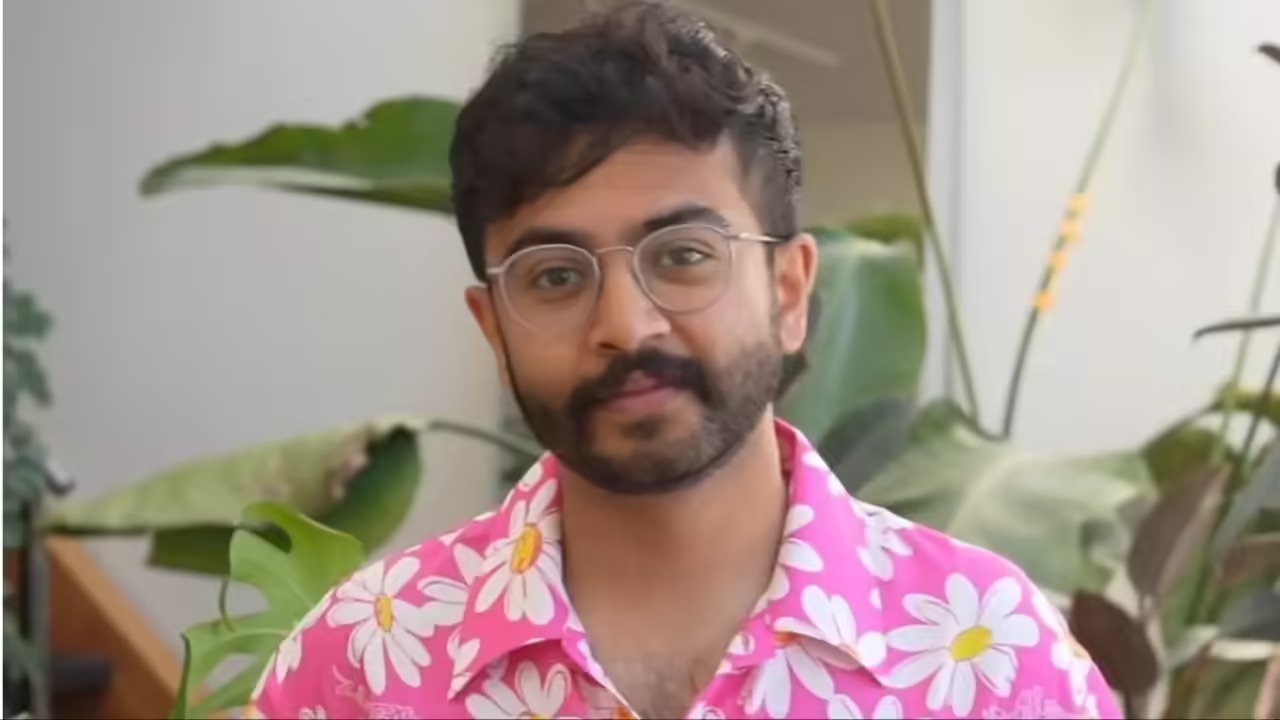 A person with glasses and a beard stands indoors, wearing a bright pink shirt with white and yellow daisy prints. Green plants are visible in the background, hinting at a fresh start—much like when Abidur Chowdhury leaves Apple.