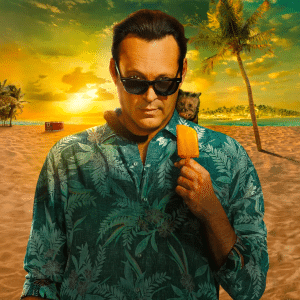 A man in sunglasses and a green tropical shirt holds an orange popsicle on a sandy beach at sunset, with palm trees, a small dog on his shoulder, and the ocean in the background—perfect vibes for fans awaiting Bad Monkey Season 2.