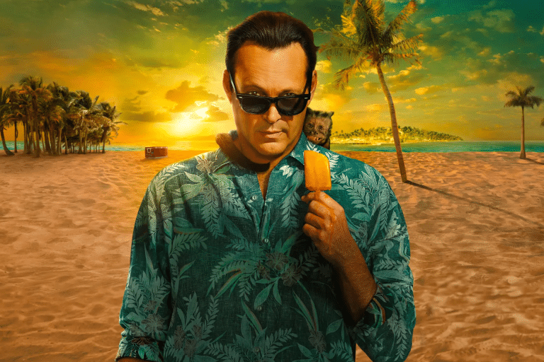 A man in sunglasses and a green tropical shirt holds an orange popsicle on a sandy beach at sunset, with palm trees, a small dog on his shoulder, and the ocean in the background—perfect vibes for fans awaiting Bad Monkey Season 2.