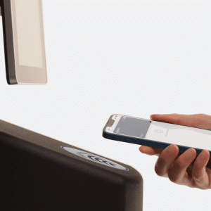 A person holds a smartphone near a payment terminal, using Apple Wallet to make a contactless transaction with their digital passport. The background is white and minimalistic.