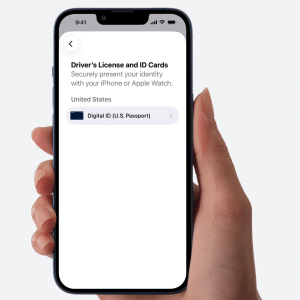 A hand holds a smartphone displaying an Apple Wallet digital passport screen for adding digital IDs, showing "Driver’s License and ID Cards" under United States with an option for "Digital ID (U.S. Passport)" on a white background.