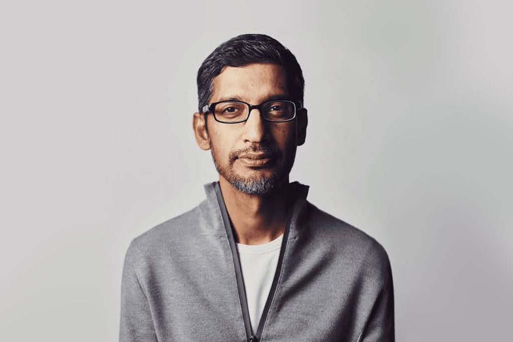 A man with short dark hair, a trimmed beard, and glasses—reminiscent of the Google CEO doomsday AI theory discussions—is wearing a light gray zip-up jacket over a white shirt, looking straight at the camera against a plain light background.
