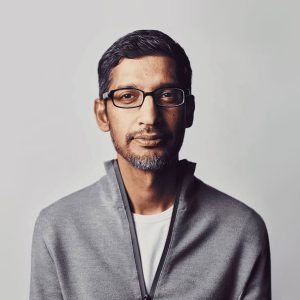 A man with short dark hair, a trimmed beard, and glasses—reminiscent of the Google CEO doomsday AI theory discussions—is wearing a light gray zip-up jacket over a white shirt, looking straight at the camera against a plain light background.