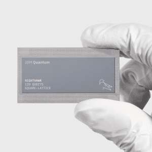 A gloved hand holds a rectangular IBM Quantum chip labeled "Nighthawk, 127 qubits, square-lattice" on a plain light background, amid swirling Apple quantum computing rumor discussions.