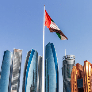 A United Arab Emirates flag on a tall pole waves in front of modern skyscrapers and blue sky in Abu Dhabi, symbolizing progress and innovation like the Microsoft UAE AI partnership.