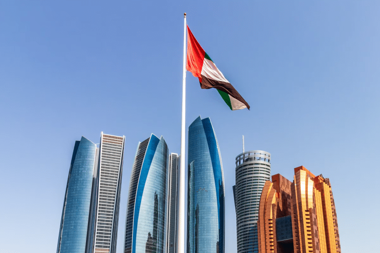 A United Arab Emirates flag on a tall pole waves in front of modern skyscrapers and blue sky in Abu Dhabi, symbolizing progress and innovation like the Microsoft UAE AI partnership.