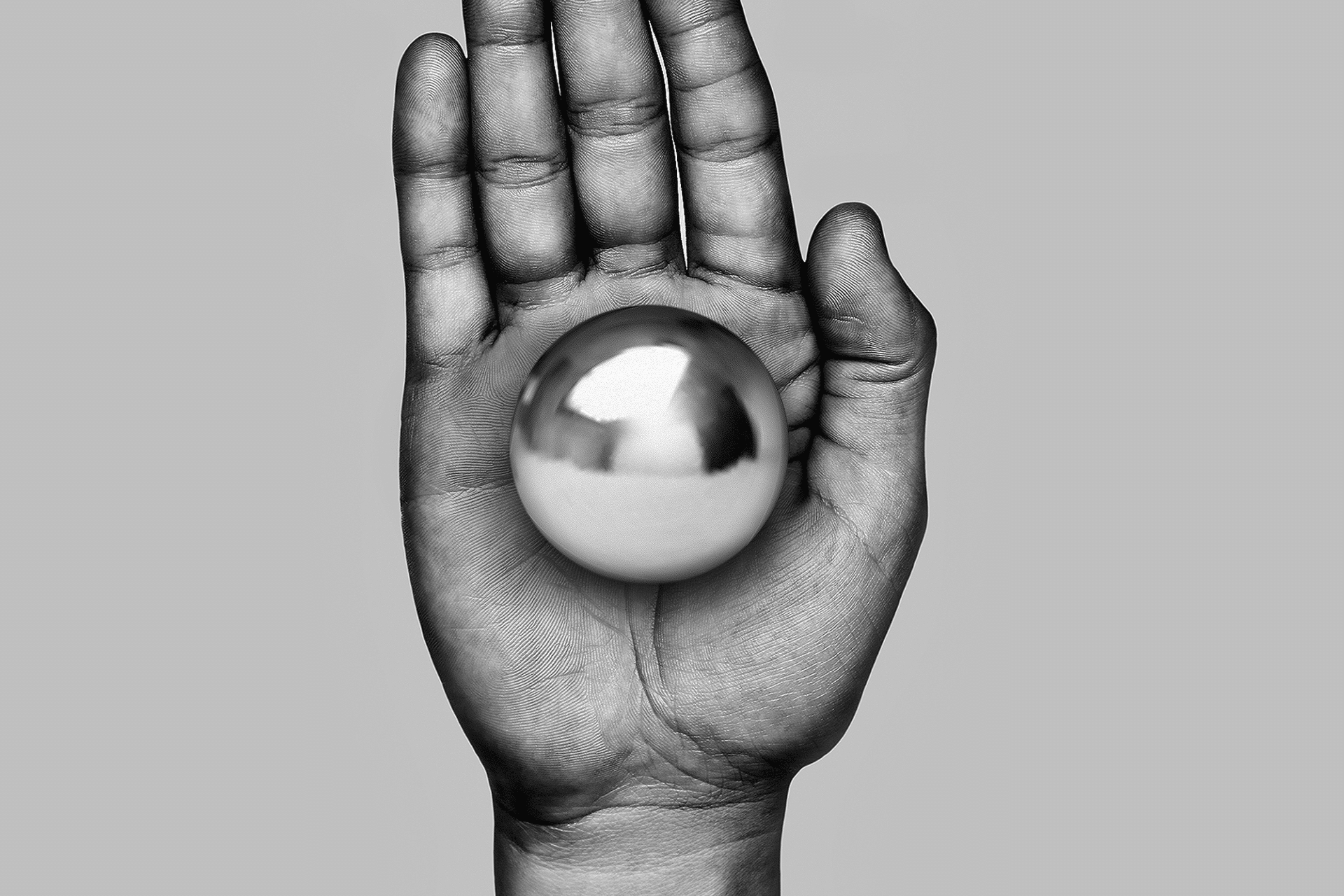 A grayscale photo of a hand held upright with the palm facing forward, holding a shiny metallic sphere—symbolizing innovation like X-Energy funding SMRs—centered in the palm against a plain gray background.