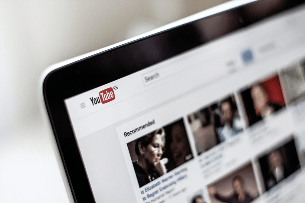 A close-up of a computer screen displaying the YouTube homepage, with the YouTube logo, search bar, and a section of recommended video thumbnails—alongside a banner promoting a YouTube TV $20 credit offer.