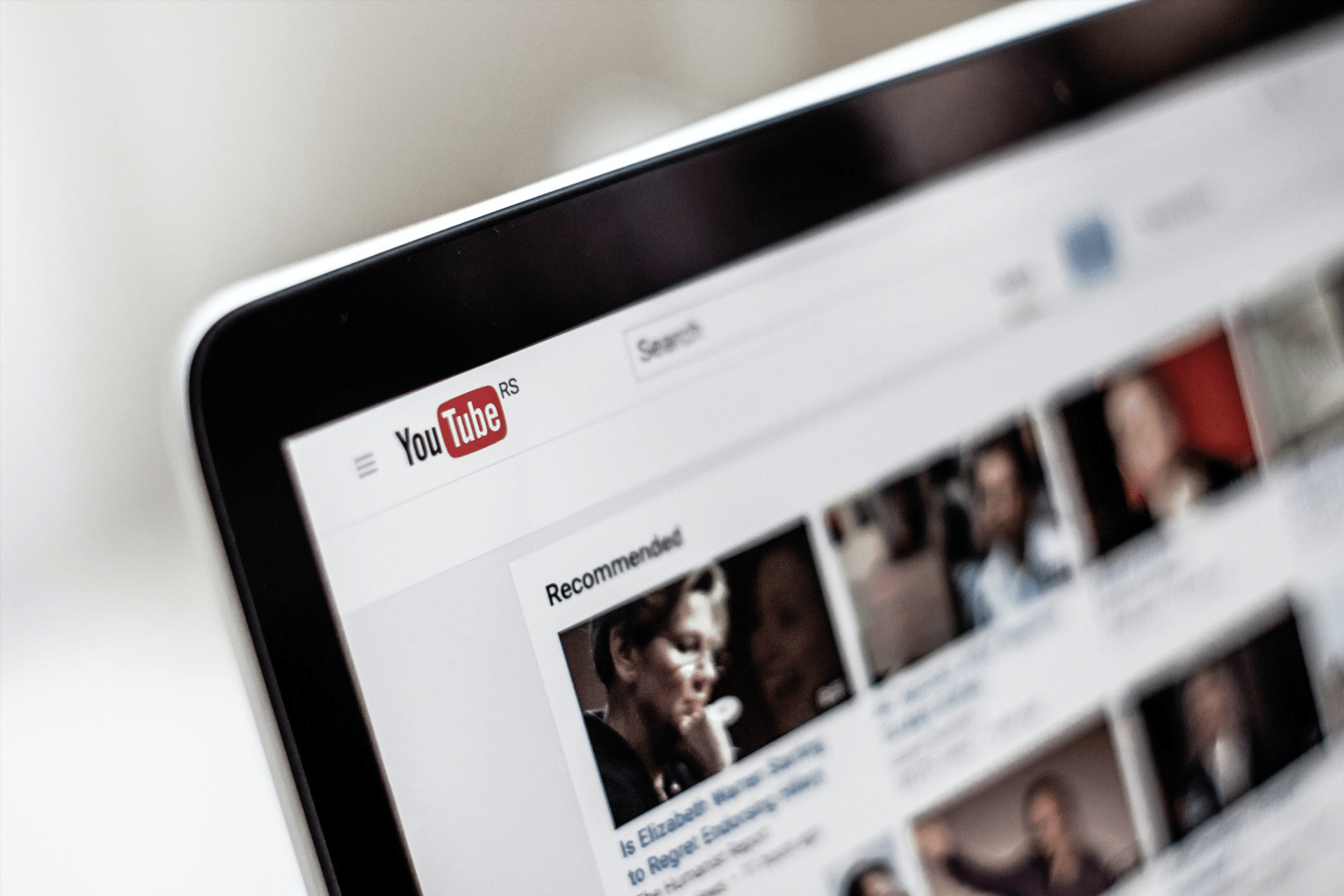 A close-up of a computer screen displaying the YouTube homepage, with the YouTube logo, search bar, and a section of recommended video thumbnails—alongside a banner promoting a YouTube TV $20 credit offer.