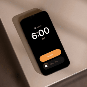A smartphone featuring the iOS 26.1 alarm slider displays a 6:00 AM alarm on a beige surface. The screen shows options to snooze or stop the alarm.