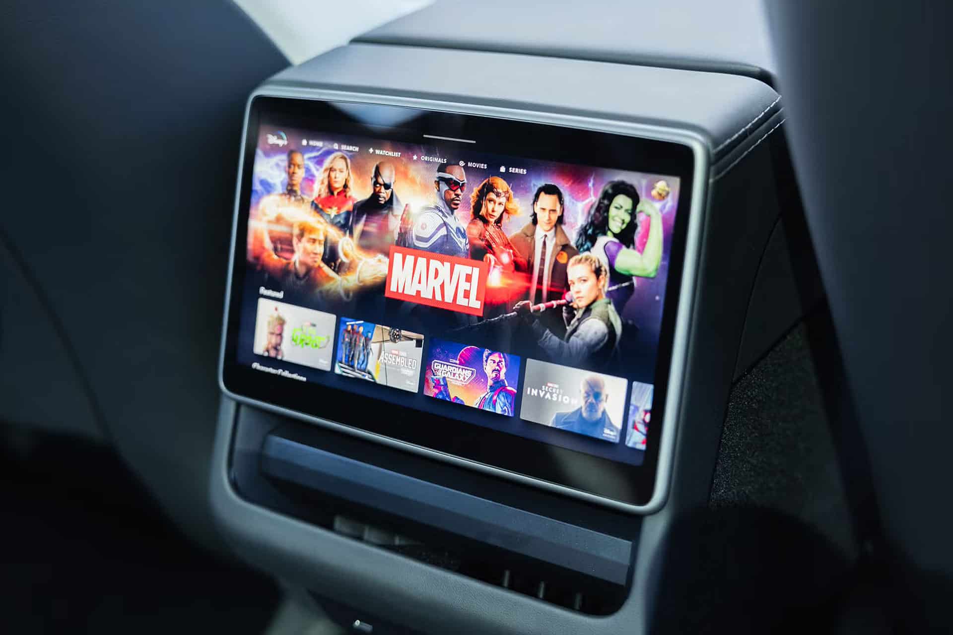A touchscreen display in a 2025 car showcases the Marvel section of a streaming service, featuring characters and movies. The screen, mounted on the back of a front seat, includes digital safety features for secure browsing.
