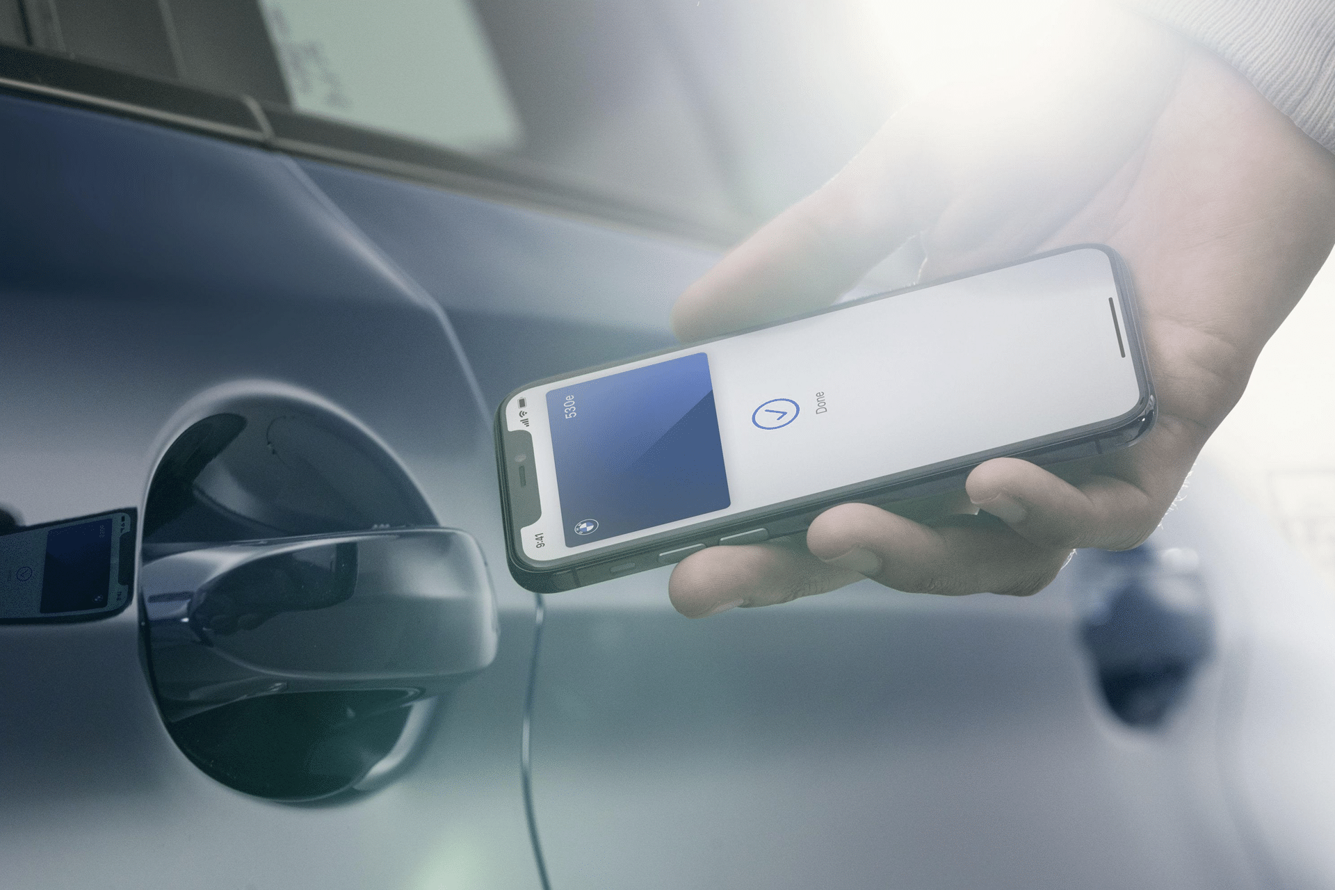 A person holds a smartphone with the Apple Car Key app open near the door handle of a blue car, preparing to unlock it using their phone. Sunlight shines onto the scene as Apple Car Key expands in 2026.