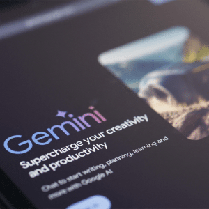 A tablet screen displays the Gemini AI homepage with the text, "Gemini: Supercharge your creativity and productivity," next to a blurred image and a dark background, highlighting its recent iOS AI expansion.