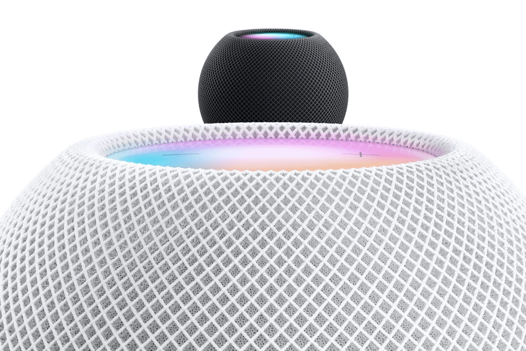 Close-up of a white mesh Apple HomePod smart speaker with its colorful touch surface glowing, and a smaller black HomePod mini speaker—perfect for those considering an Apple HomePod mini upgrade—placed on top.