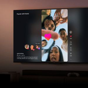 A TV screen shows an Instagram Reels vertical video of five young people looking down at the camera with a pink heart icon. On the left, Fire TV displays comments, likes, and engagement stats. The dim room reveals part of a colorful painting.