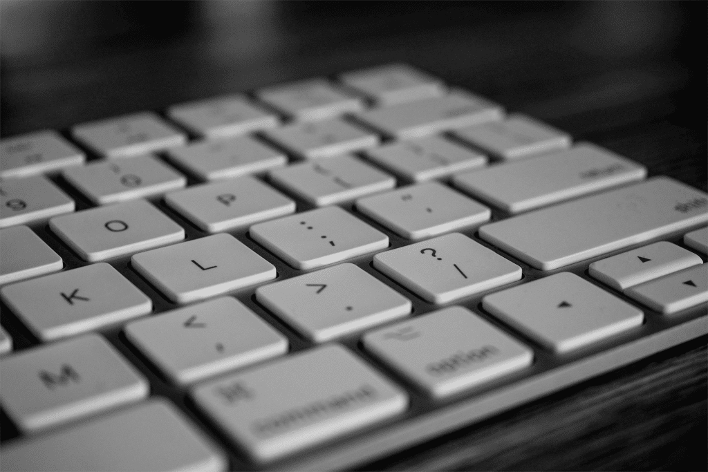 A close-up, black and white image of a Magic Keyboard focusing on the central letter and symbol keys, with shallow depth of field and a blurred background.